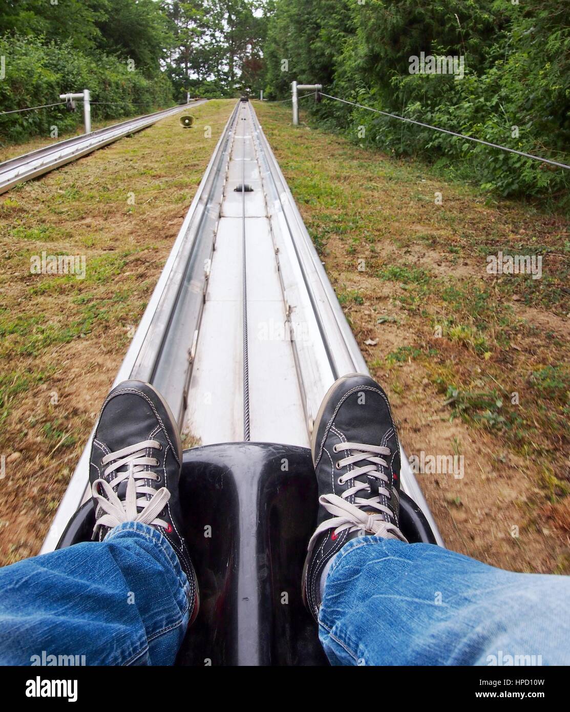 Point of view shot at summer bobsled track. View on the legs and the bobsled tobbogan elevator during rising up the hill. POV Stock Photo