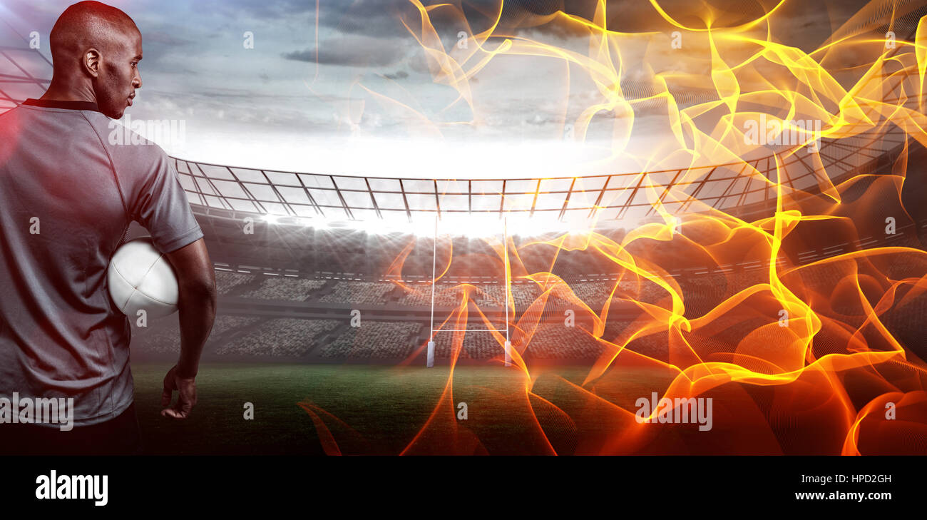 Abstract orange glowing black background against rear view of sportsman with rugby ball Stock Photo