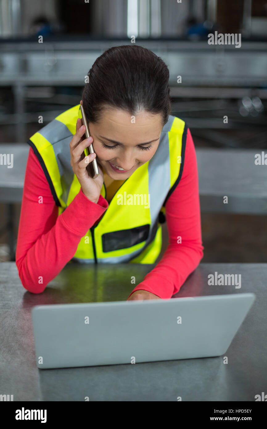 Female factory worker using laptop while talking on mobile phone at ...