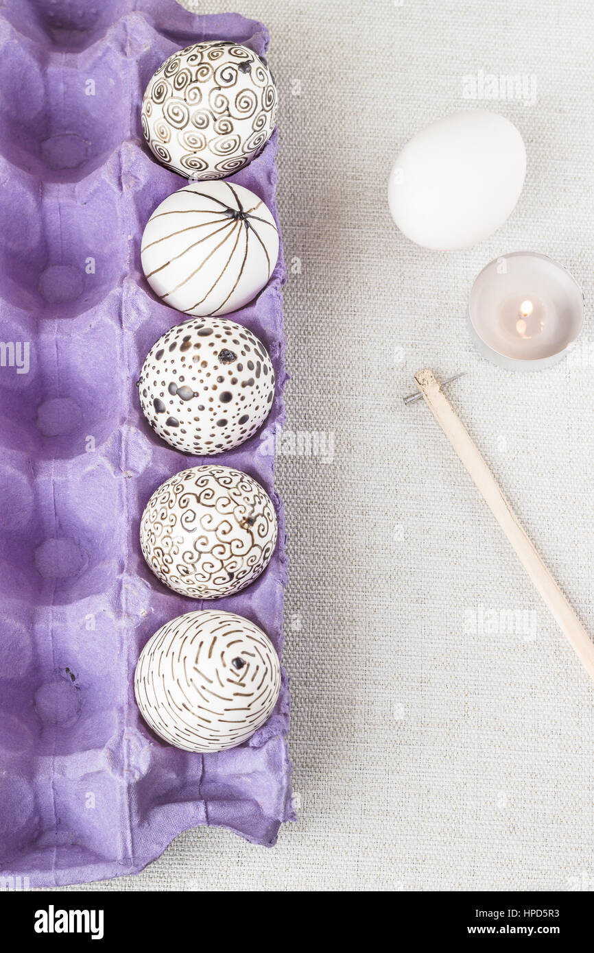 Decorating Easter eggs using a traditional wax-resist method and modern patterns. Eggs in a purple paper box with molten wax applied to the white shel Stock Photo