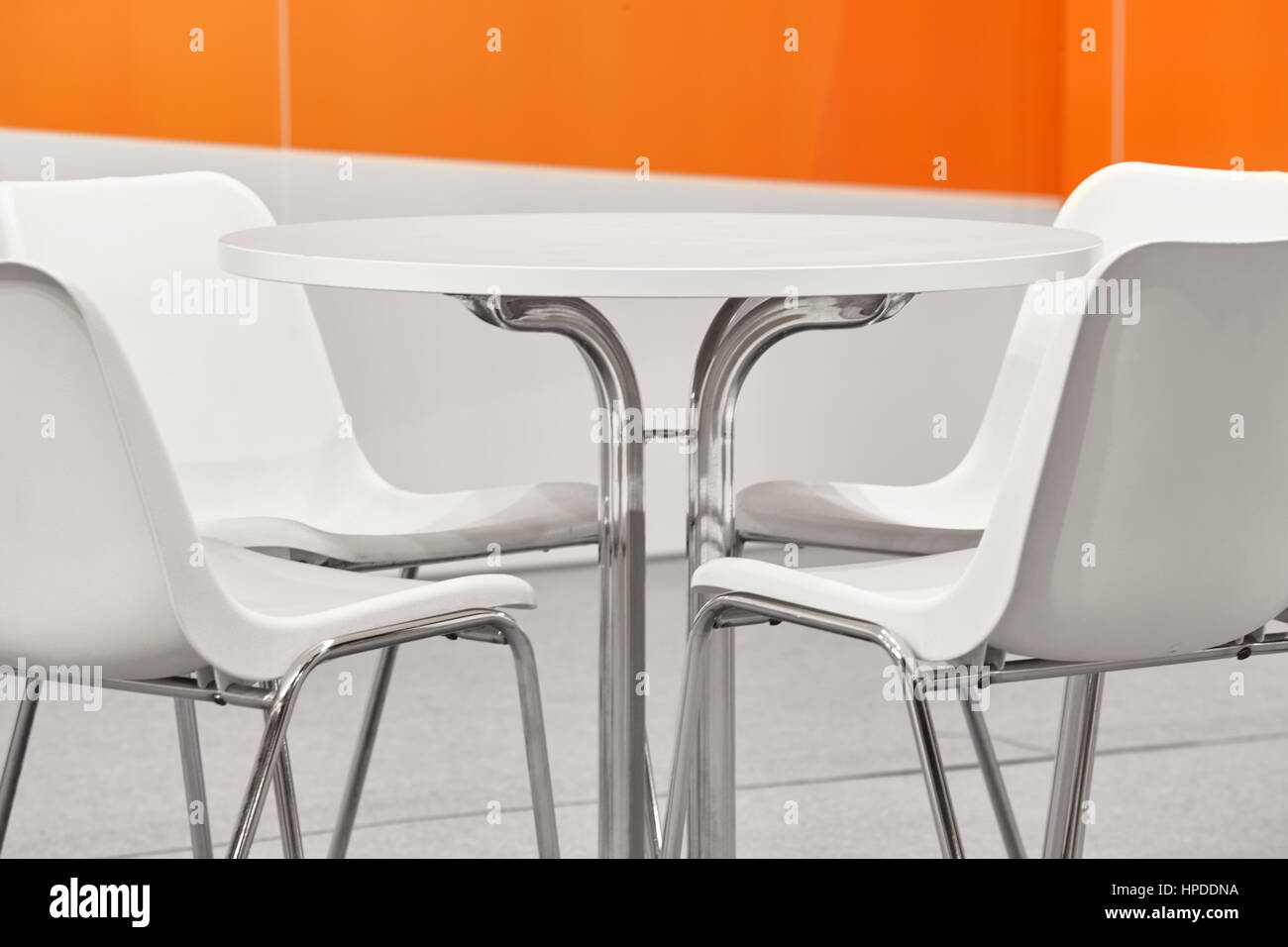 White plastic chairs and table set. Orange wall decoration. Horizontal