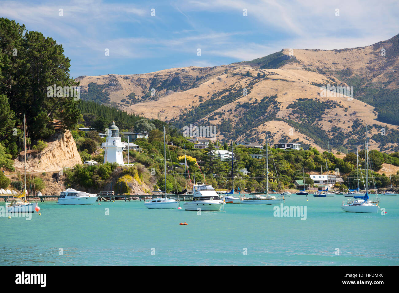 Akaroa, Canterbury, New Zealand. View across the turquoise waters of Akaroa Harbour, historic lighthouse prominent. Stock Photo