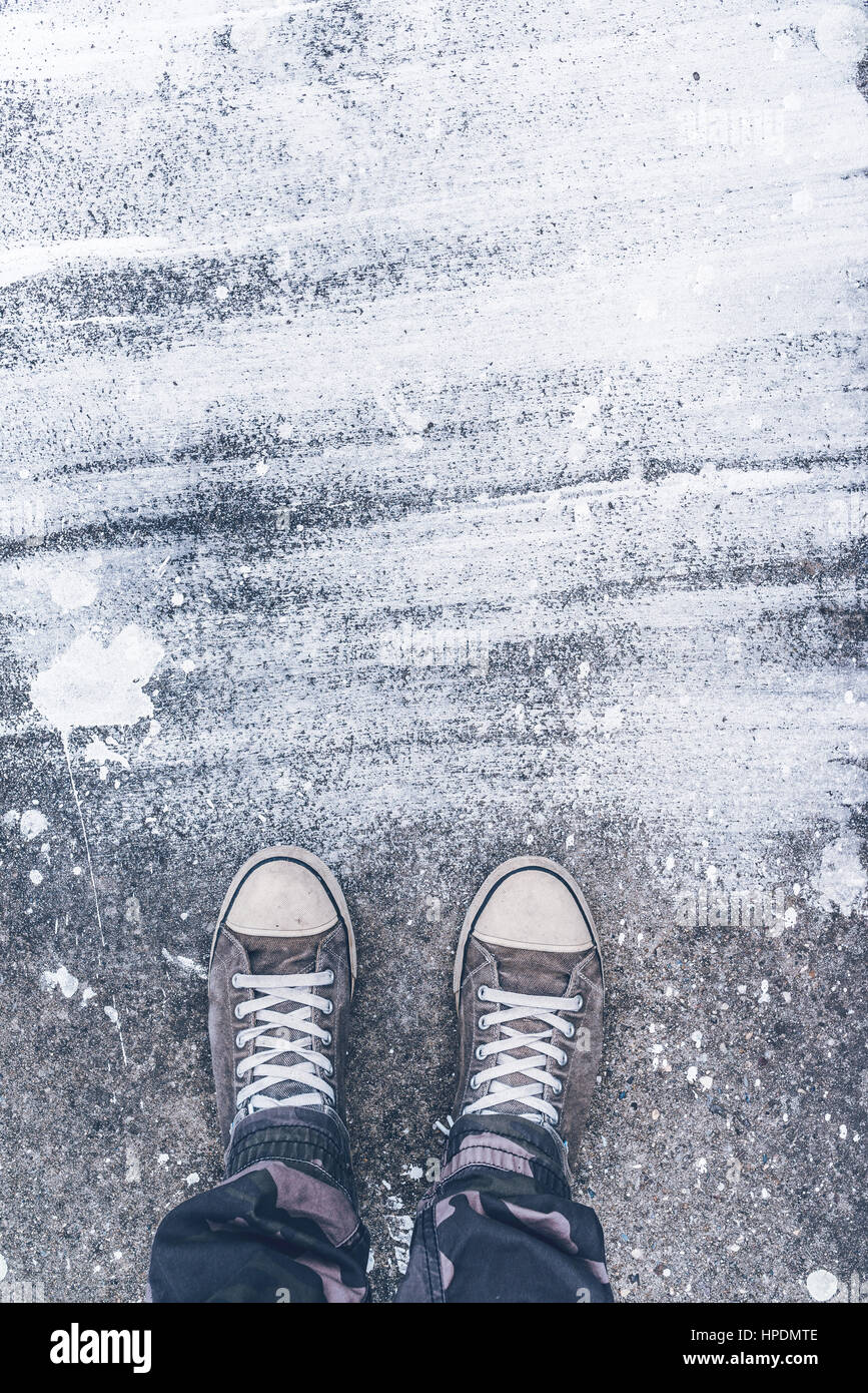 Standing on concrete floor with white drybrush stains, male feet in worn sport shoes on the street Stock Photo