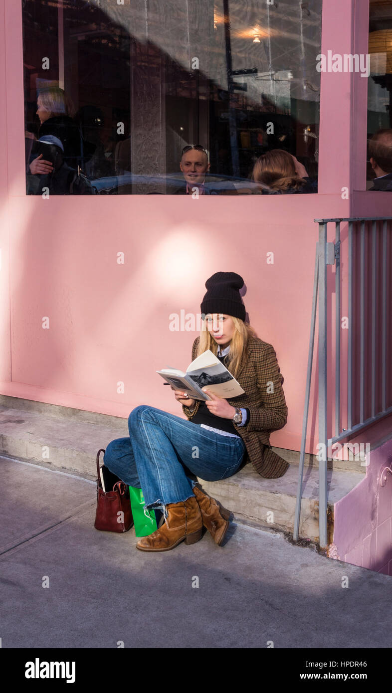 Stylish young woman reading a hard cover book while waiting for a table in a restaurant Stock Photo