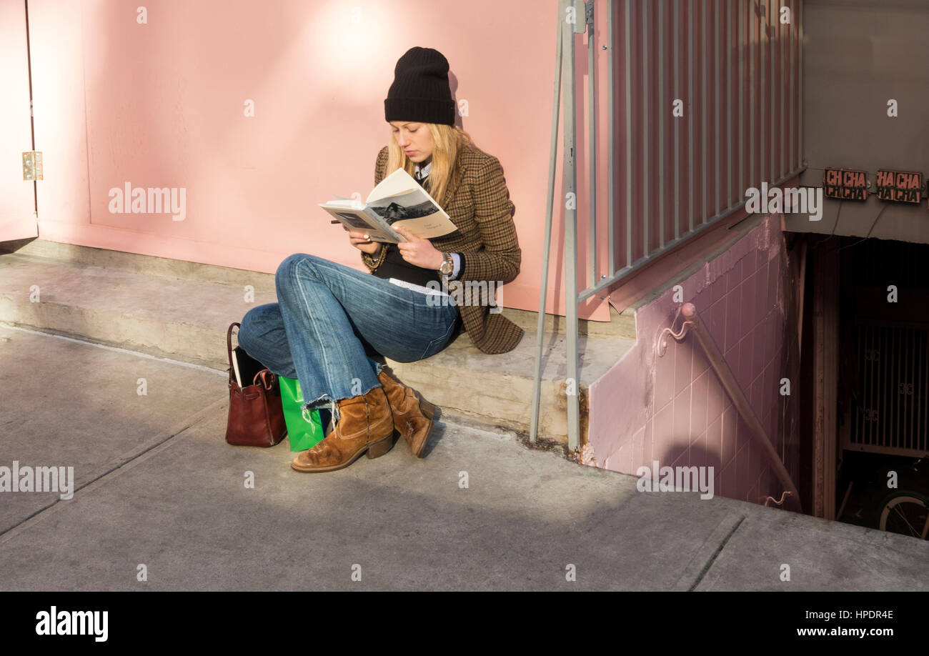 Stylish young woman reading a hard cover book while waiting for a table in a restaurant Stock Photo
