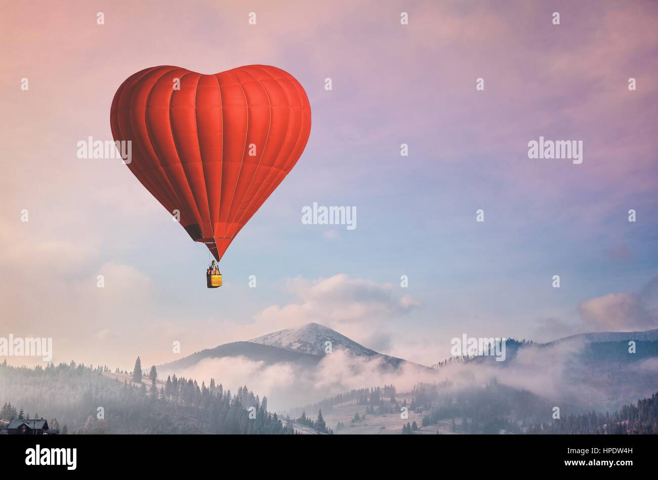 Red air balloon heart shape against blue and pink pastel sky in a sunny bright morning. Foggy mountains in the background. Romantic postcard backgroun Stock Photo
