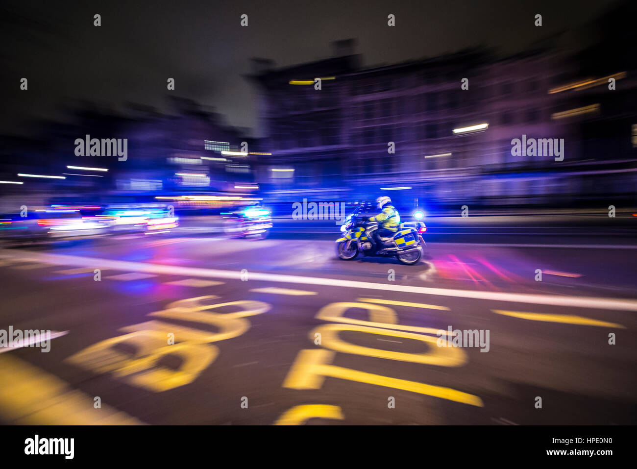 A police motorcycle racing to an incident at night along Whitehall, London, UK, with blue lights flashing. Motion blur. Police units at speed Stock Photo