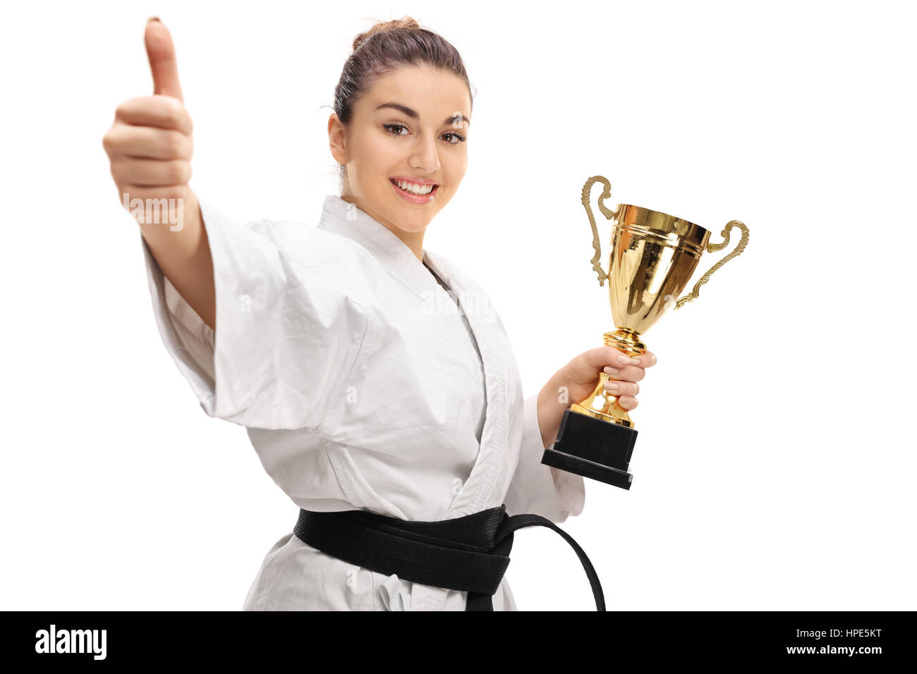 Happy karate girl giving a thumb up and holding a golden trophy isolated on white background Stock Photo