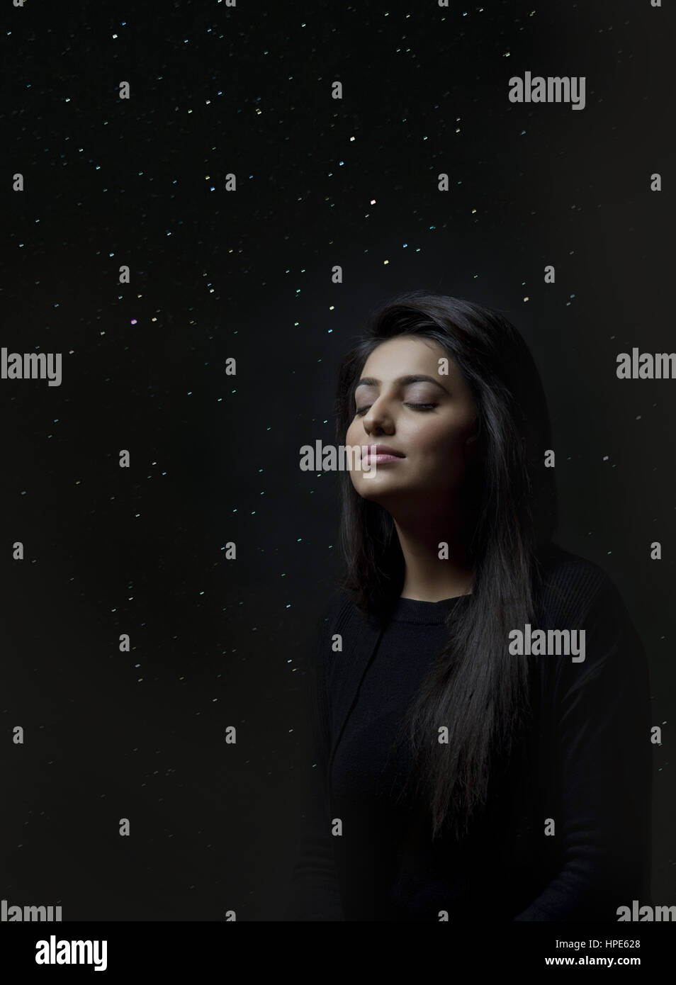 Woman thinking with closed eyes against background of glowing lights or starry sky Stock Photo