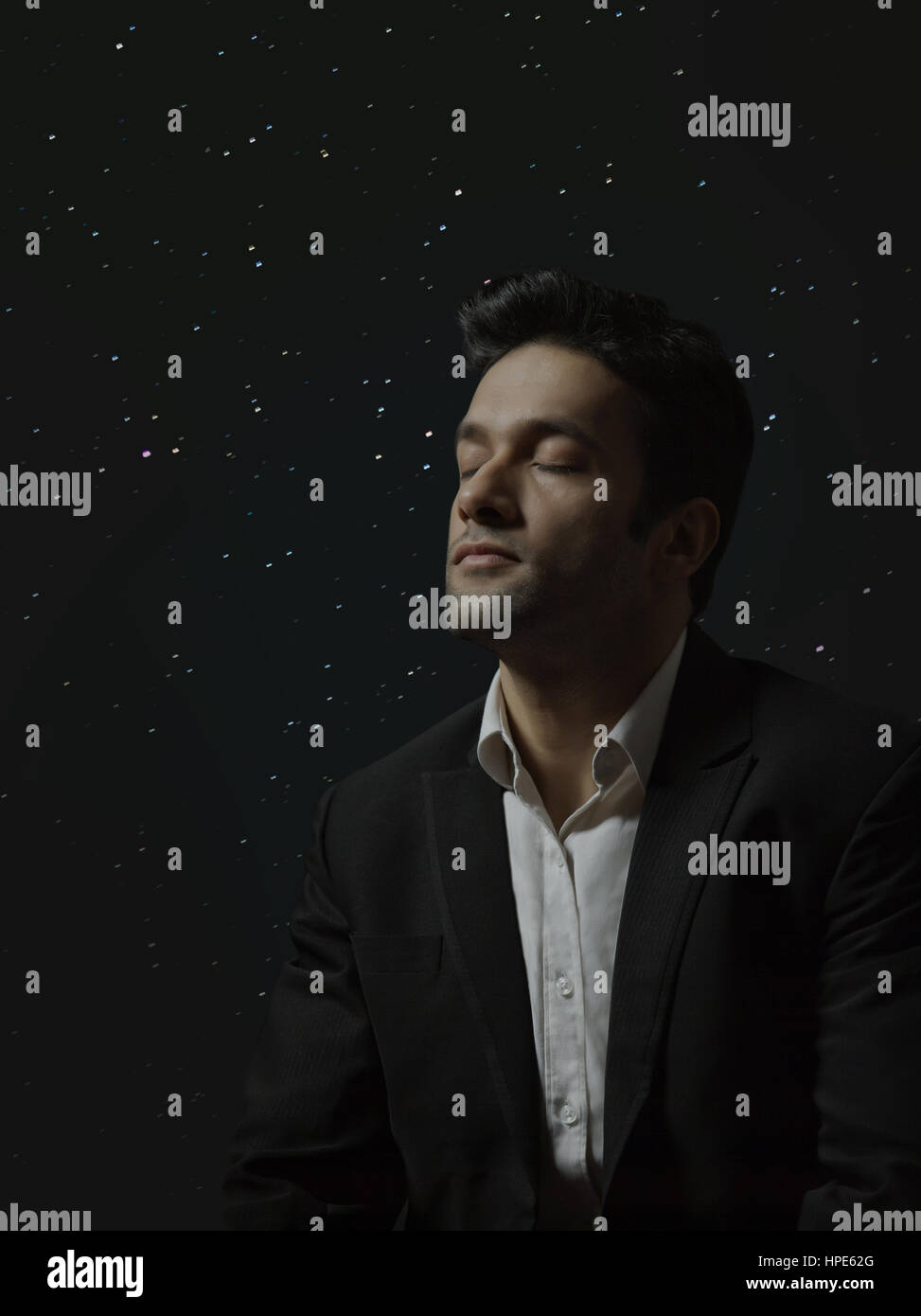 Man thinking with closed eyes against background of glowing lights or starry sky Stock Photo