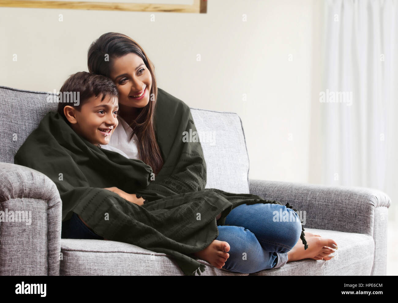 Smiling mother and son wrapped in blanket watching TV on living room
