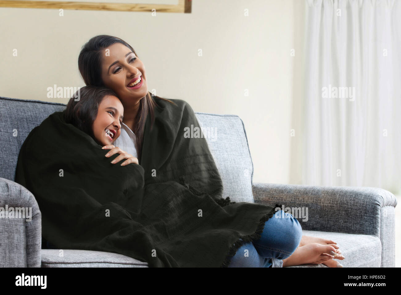 Smiling mother and daughter wrapped in blanket watching TV on living