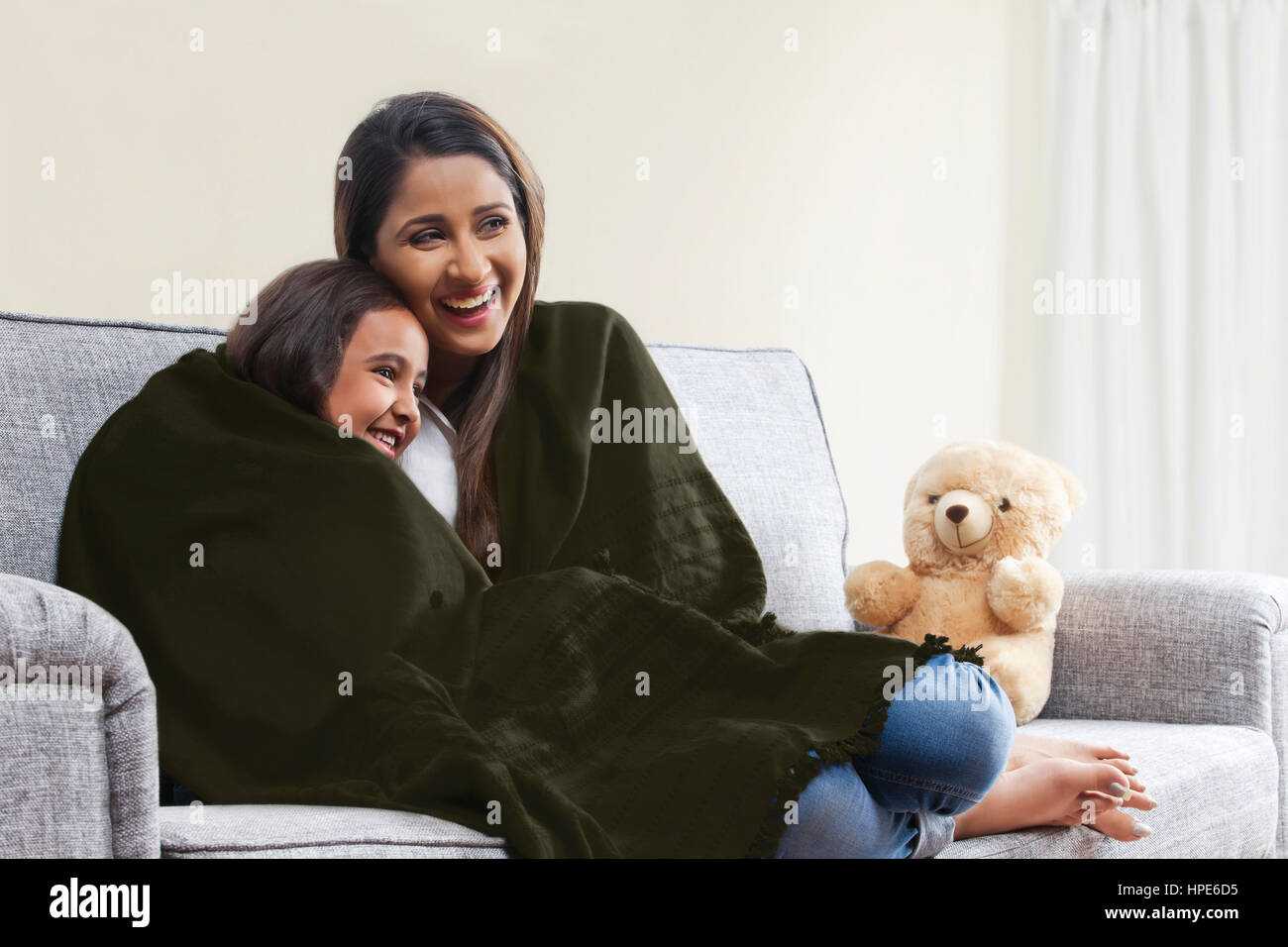 Smiling mother and daughter wrapped in blanket watching TV on living