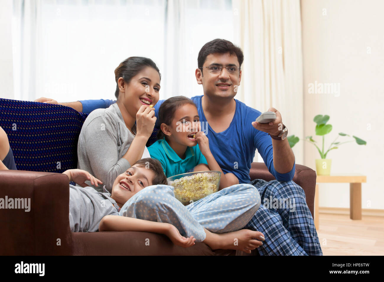 Smiling young family watching television together and eating popcorn Stock Photo
