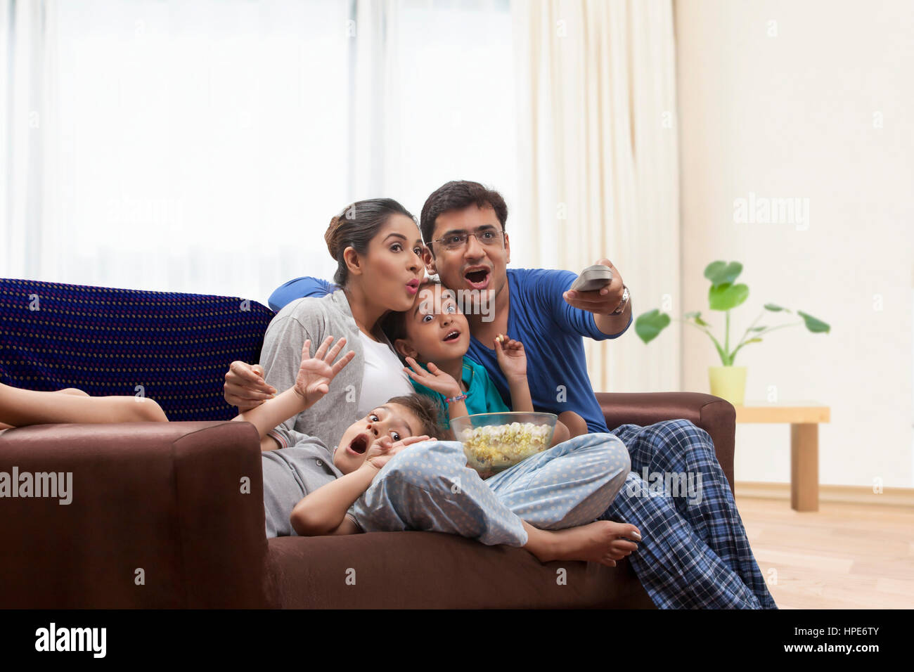 Family in pyjamas watching TV and eating popcorn Stock Photo