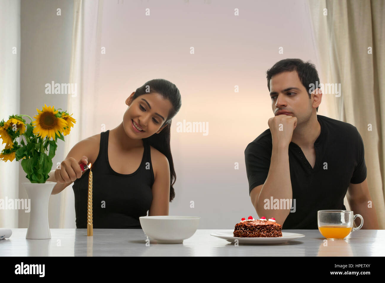 Serious man looking at woman lighting candle at table with cake Stock Photo