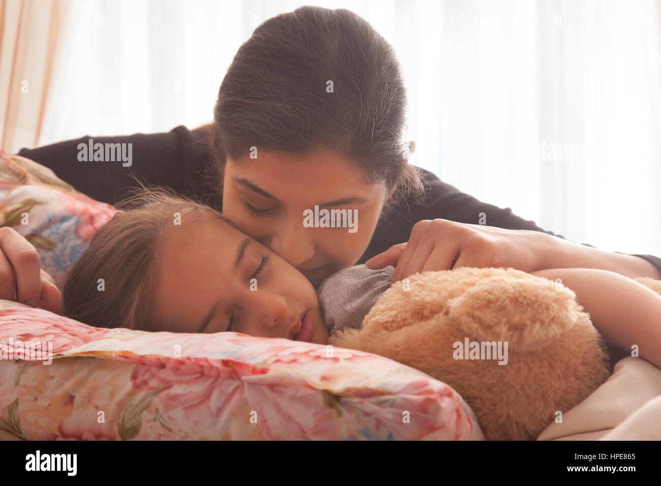 Woman kissing sleeping daughter in bed Stock Photo - Alamy