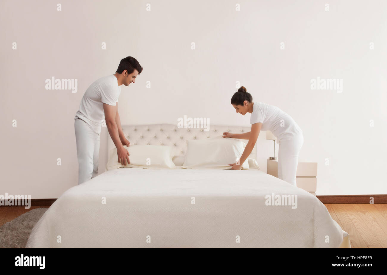 Couple making bed in bedroom Stock Photo