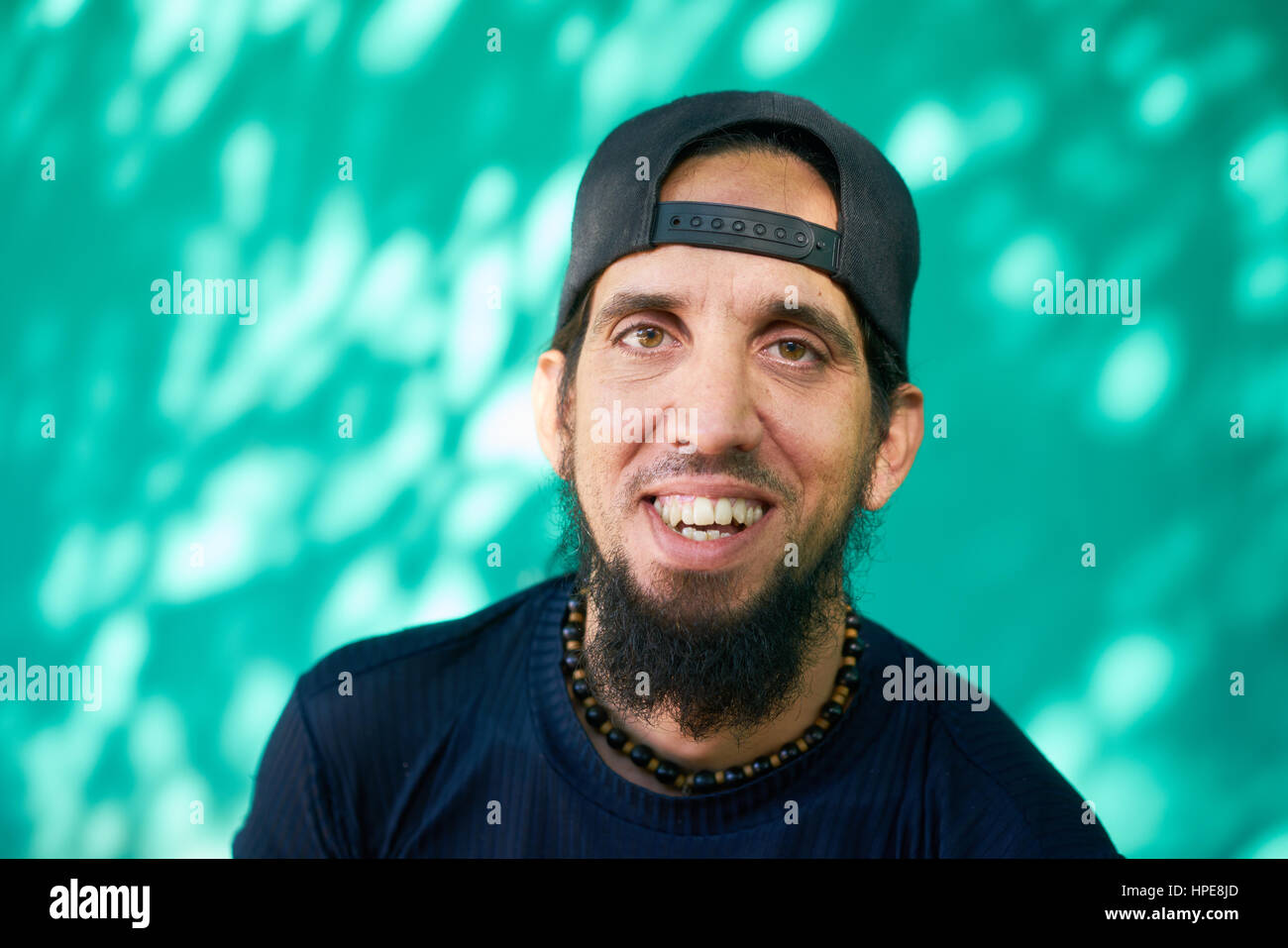 Real Cuban people and feelings, portrait of happy hispanic man with beard, baseball cap and long hair from Havana, Cuba looking at camera and laughing Stock Photo