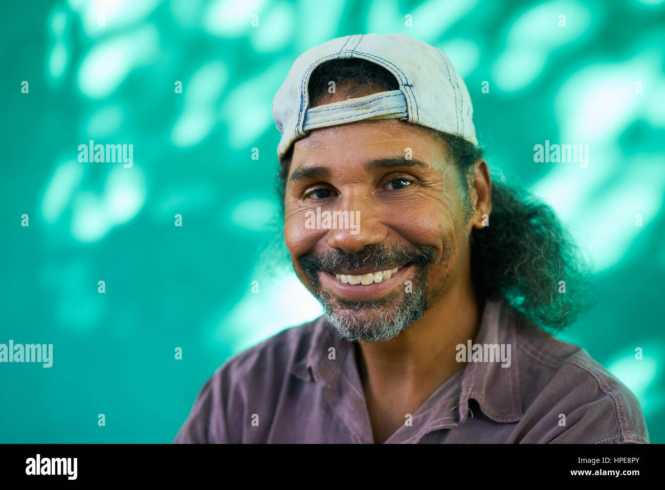 Real Cuban people and feelings, portrait of happy hispanic man with goatee, baseball cap and long hair from Havana, Cuba looking at camera and laughin Stock Photo