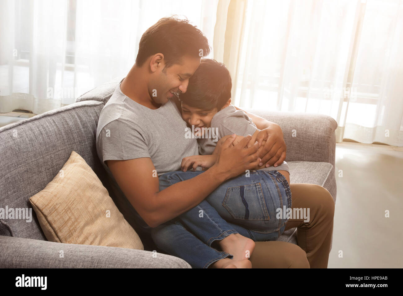 Father holding son in his lap sitting on sofa Stock Photo