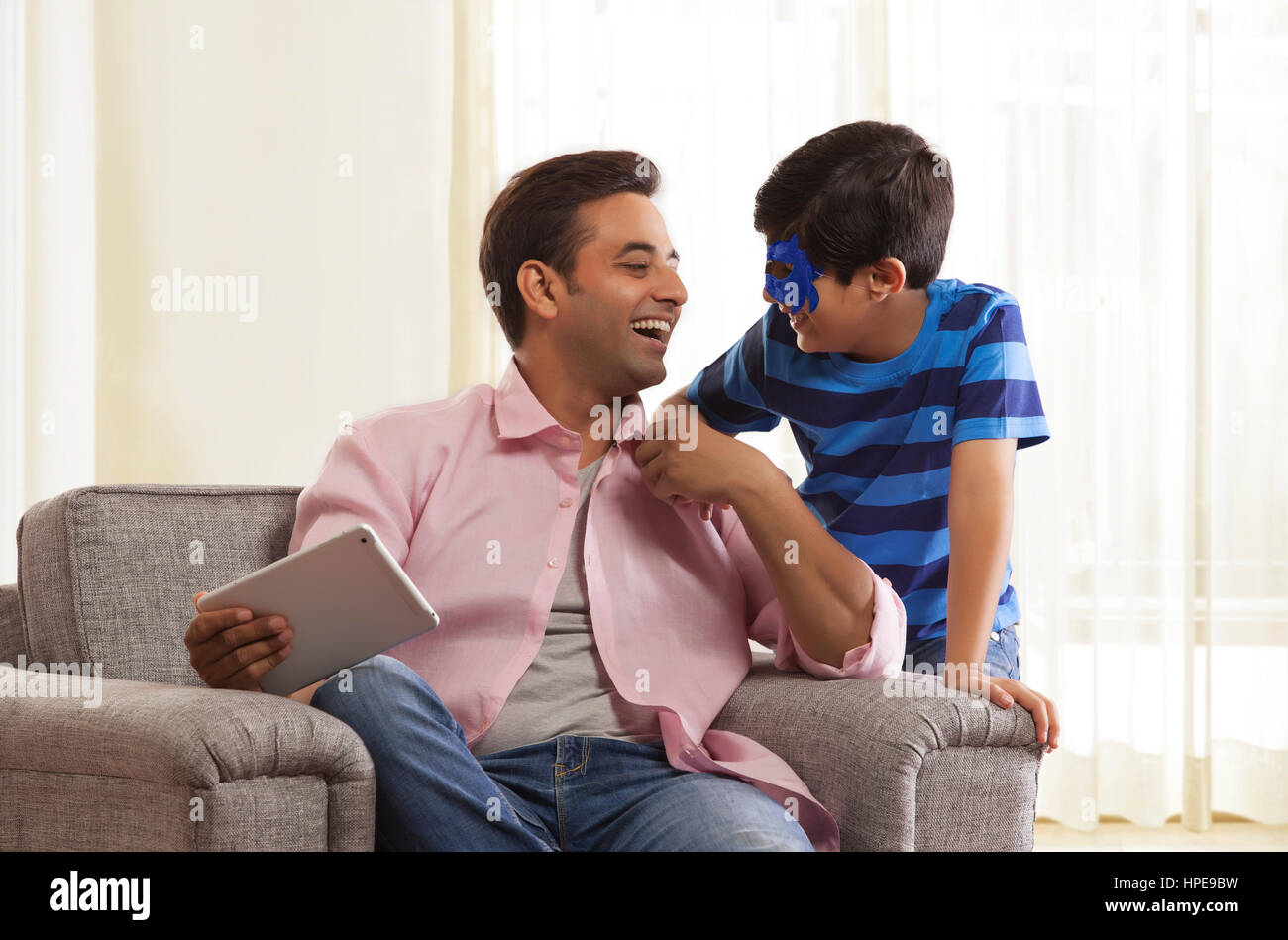 Boy with face mask laughing with his father looking at each other Stock Photo