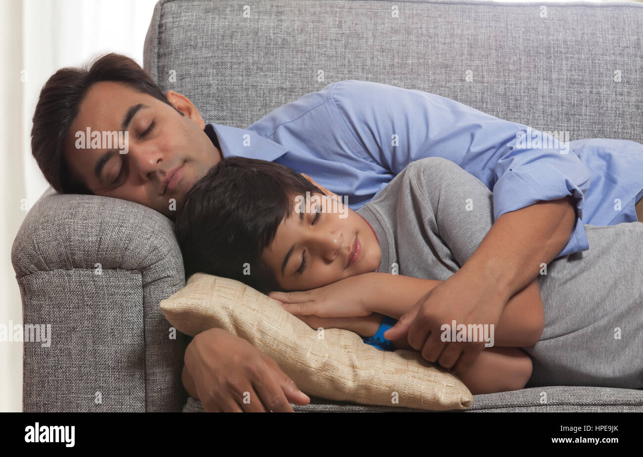 Tired father and son sleeping together on sofa at home Stock Photo