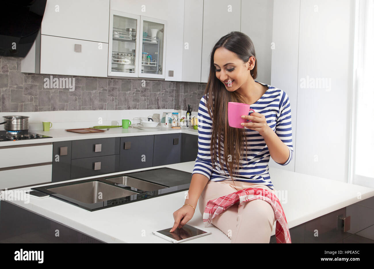 Young woman holding cup of tea using digital tablet in kitchen Stock Photo