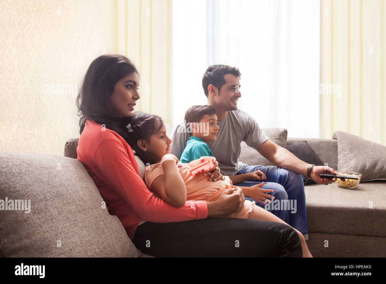 Parents with son and daughter sitting on sofa and watching TV Stock Photo