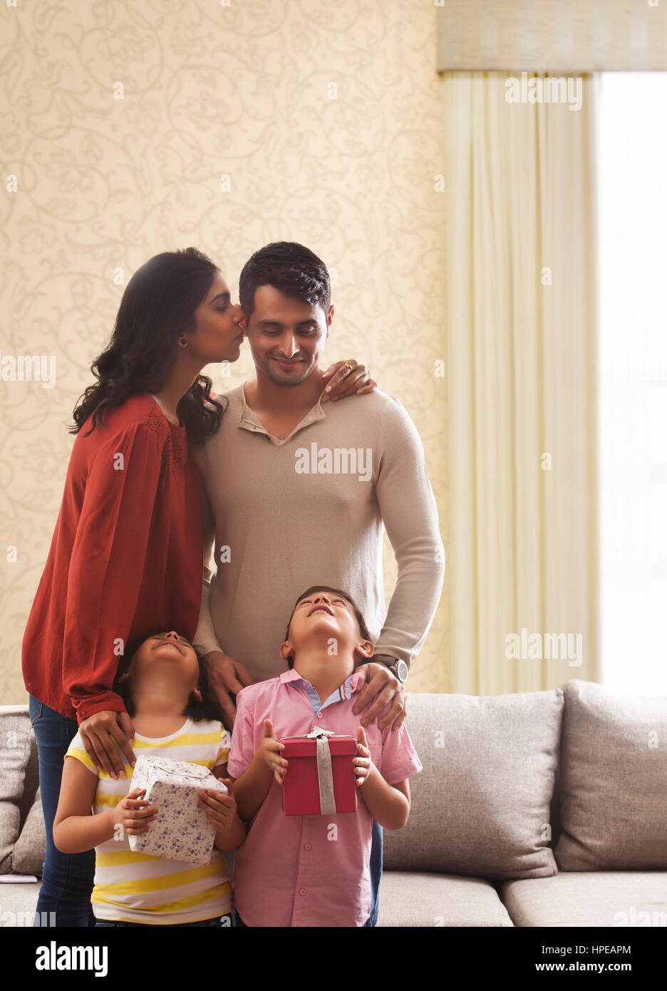 Woman kissing man on cheek, girl and boy holding gifts looking up with heads back Stock Photo