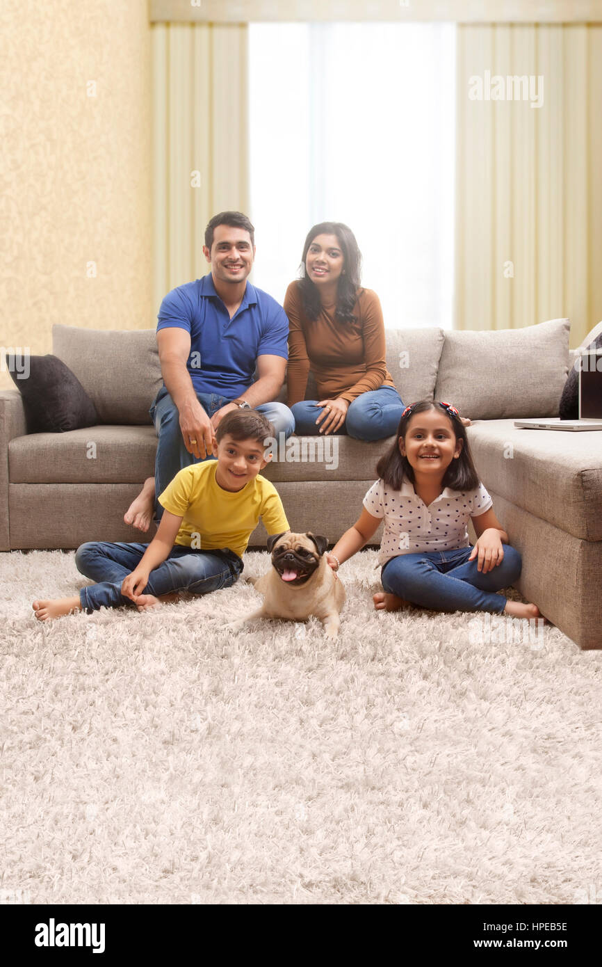 Two children playing with pug on floor and parents sitting on sofa Stock Photo