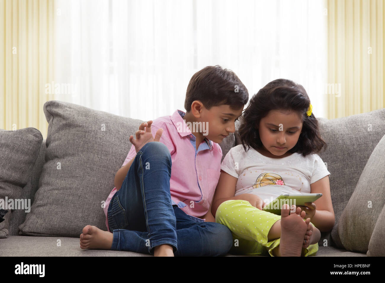 Brother and sister sitting on sofa using digital tablet Stock Photo - Alamy