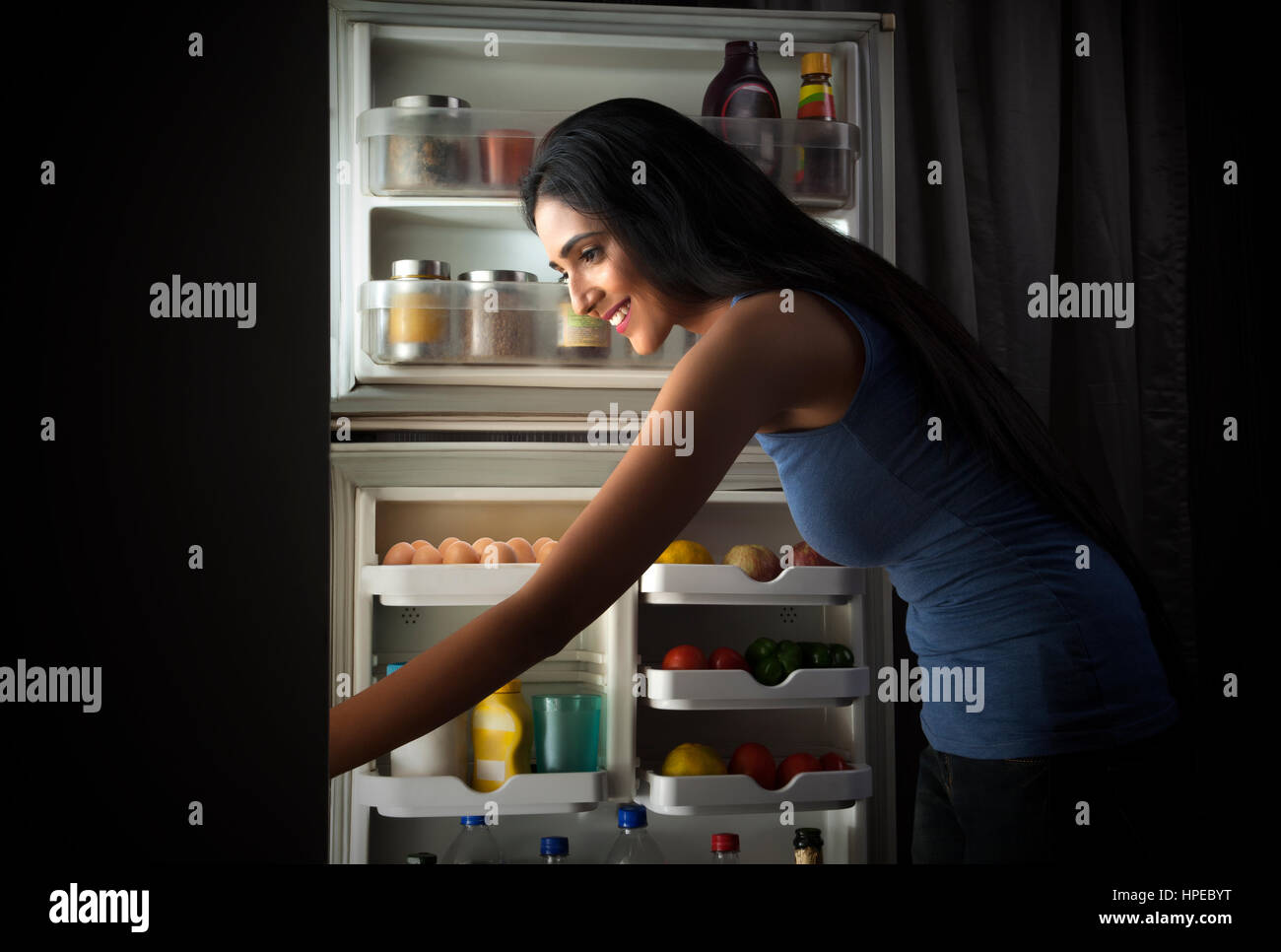 Smiling young woman looking in the fridge at night Stock Photo