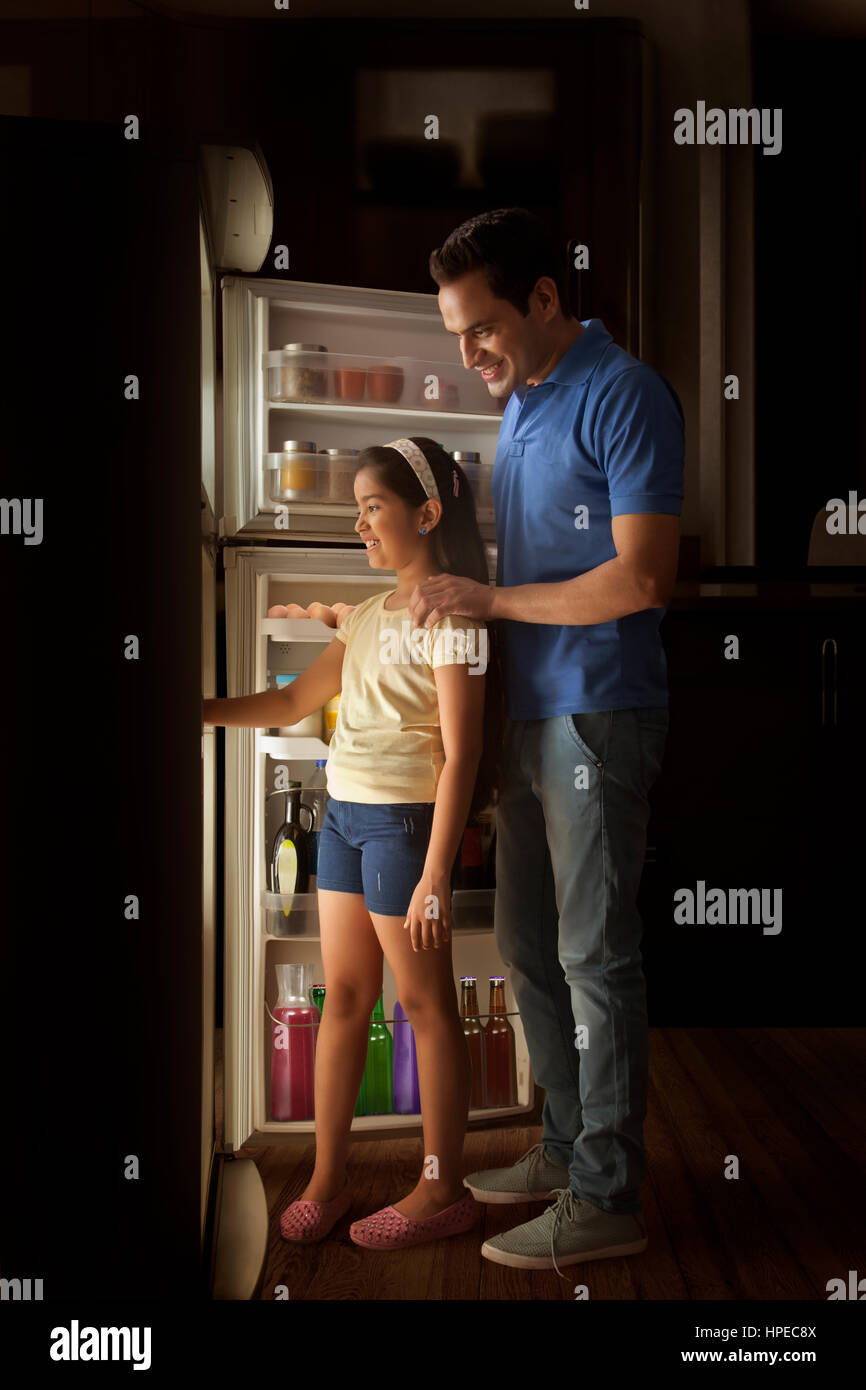 Father and daughter searching food in fridge at night Stock Photo