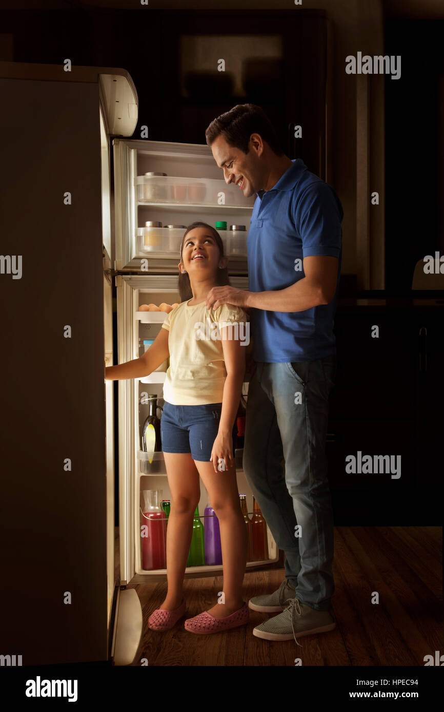 Father and daughter opening fridge at night Stock Photo