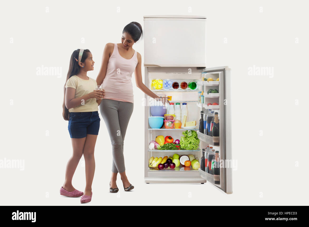 Daughter holding glass of water and mother pointing at refrigerator Stock Photo