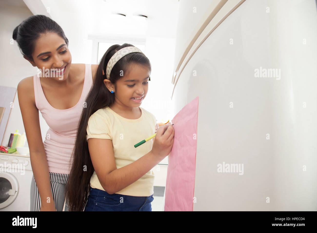Mother looking at daughter writing note on refrigerator Stock Photo