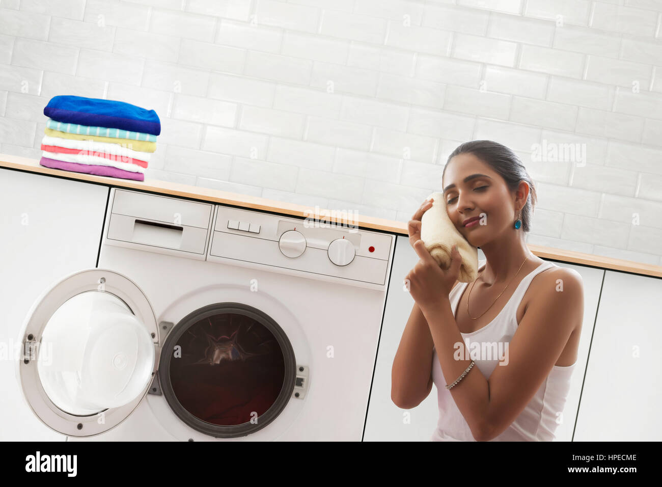 Young woman holding laundry at face in front of washing machine Stock Photo