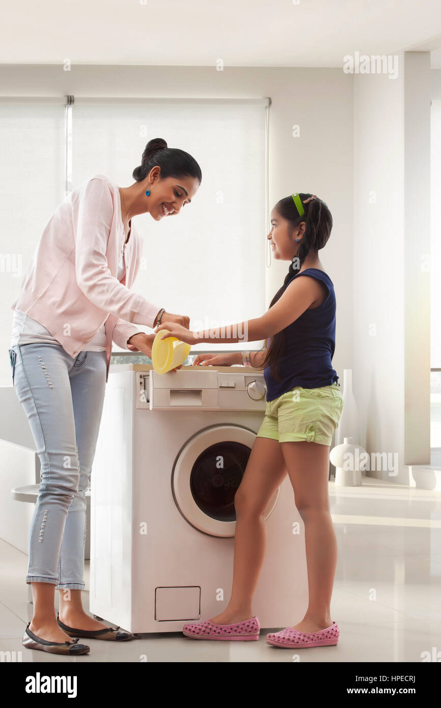 Mother and daughter pouring liquid detergent in washing machine Stock Photo