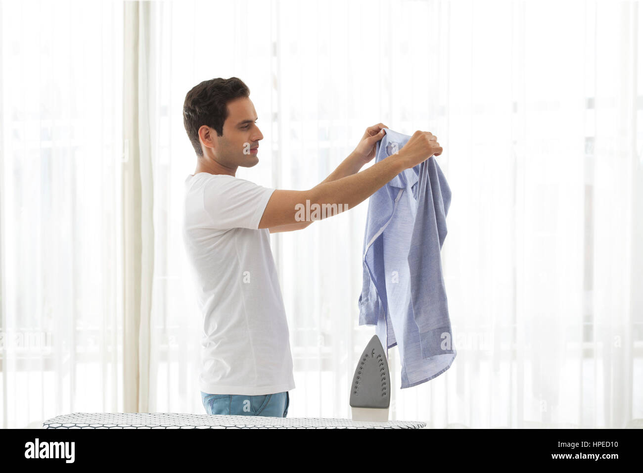 Young man looking at shirt with ironing board in front Stock Photo