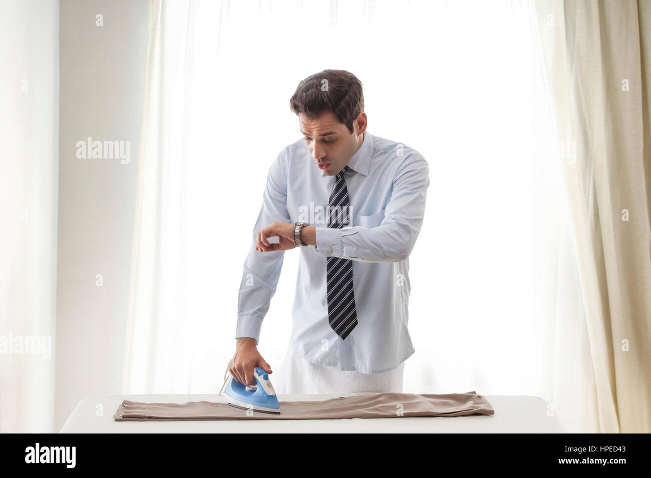 Businessman ironing pant and looking at wrist watch Stock Photo