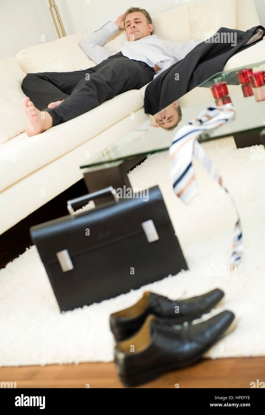 Model released , Feierabend, Geschaeftsmann liegt erschoepft Zuhause auf der Couch - end of the work day, exhausted businessman after work at home Stock Photo