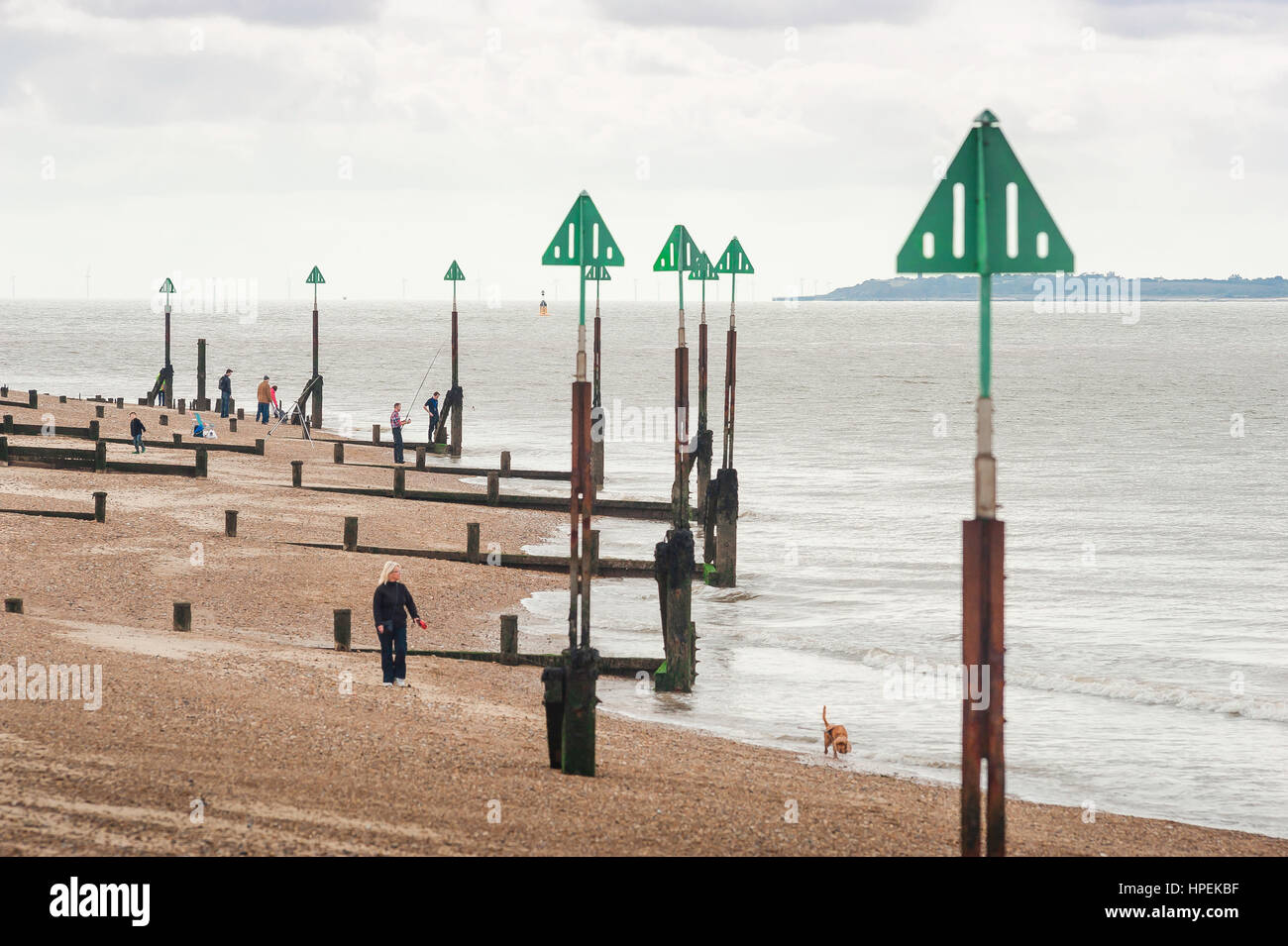 Suffolk coast UK, people walk among the tide posts on the shingle beach