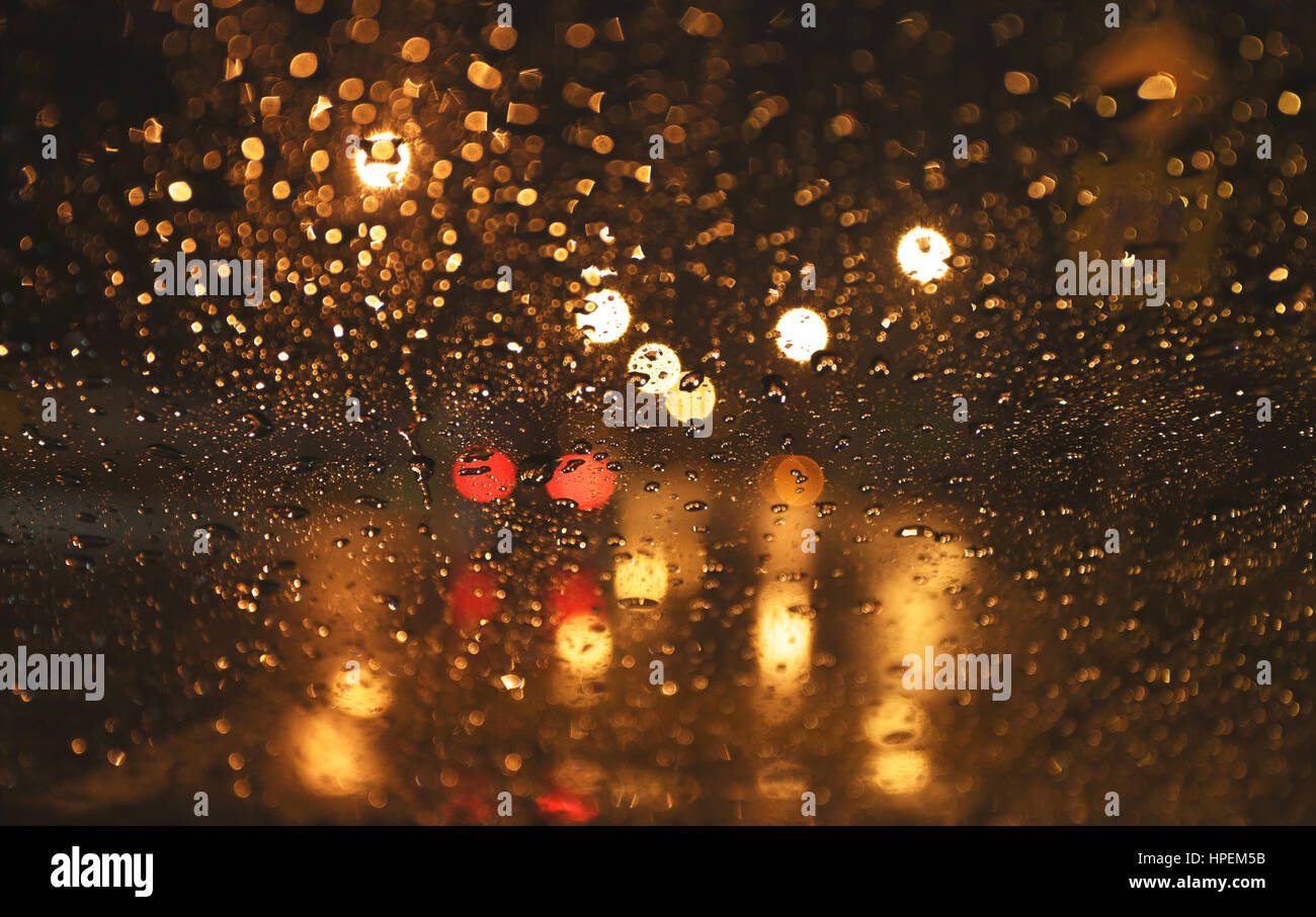 yellow street lights in blurred rain background view through wet car