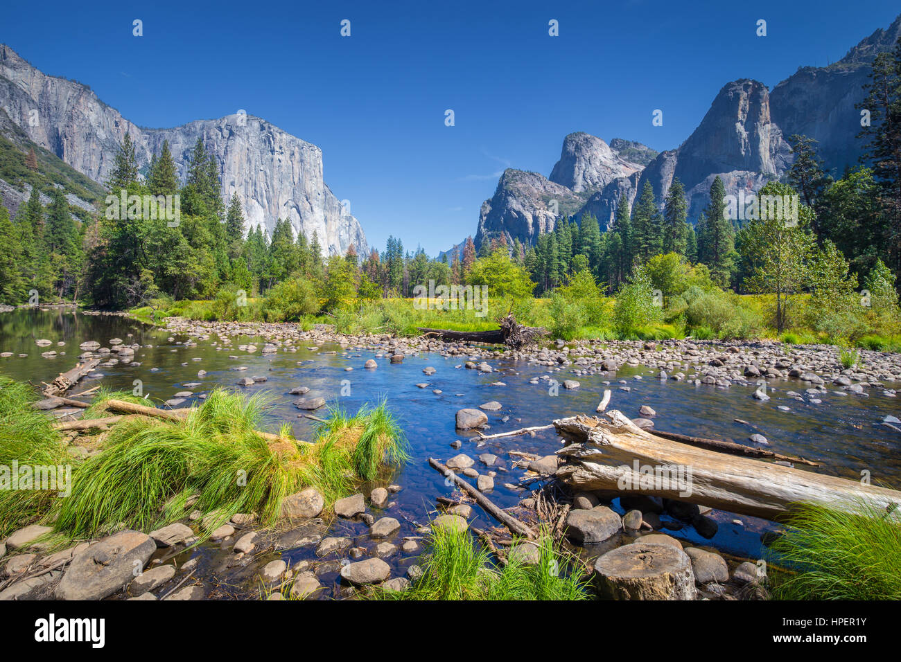Classic view of scenic Yosemite Valley with famous El Capitan rock climbing summit and idyllic Merced river on a sunny day with blue sky and clouds in Stock Photo
