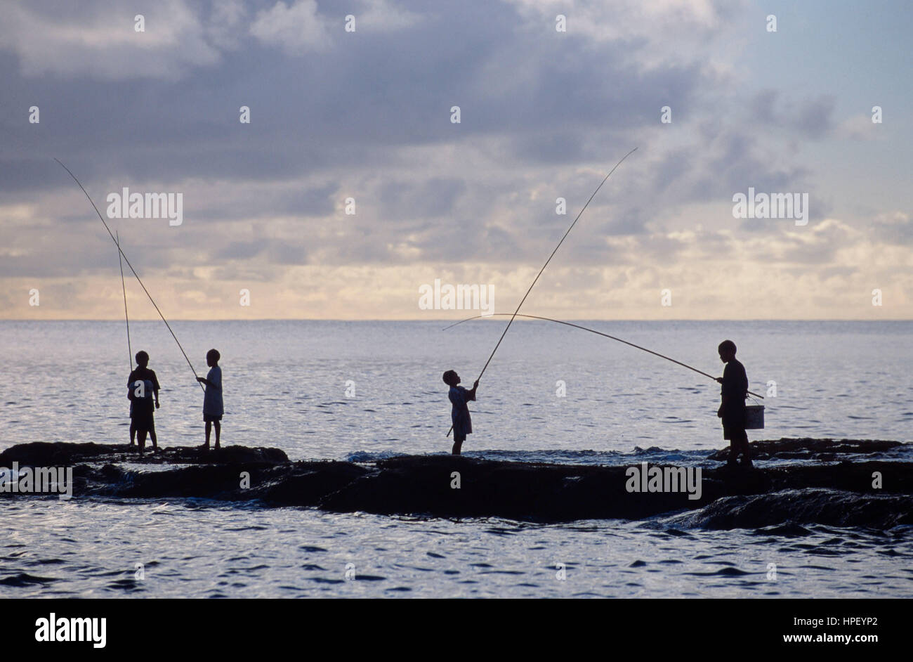 Four children with fishing rods on a rock in the sea Stock Photo