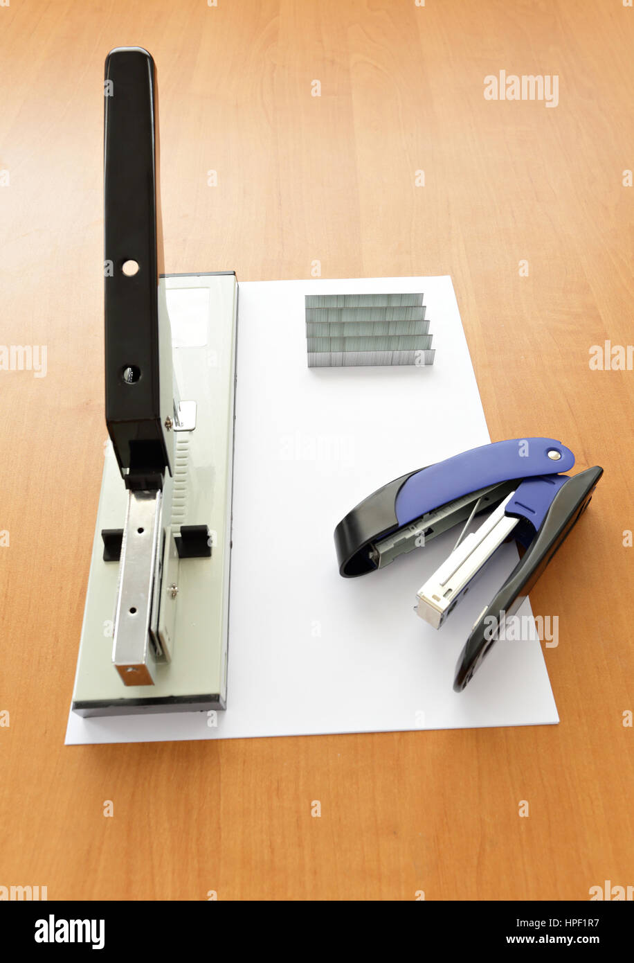 Big and small staplers with staples and paper on wood table Stock Photo