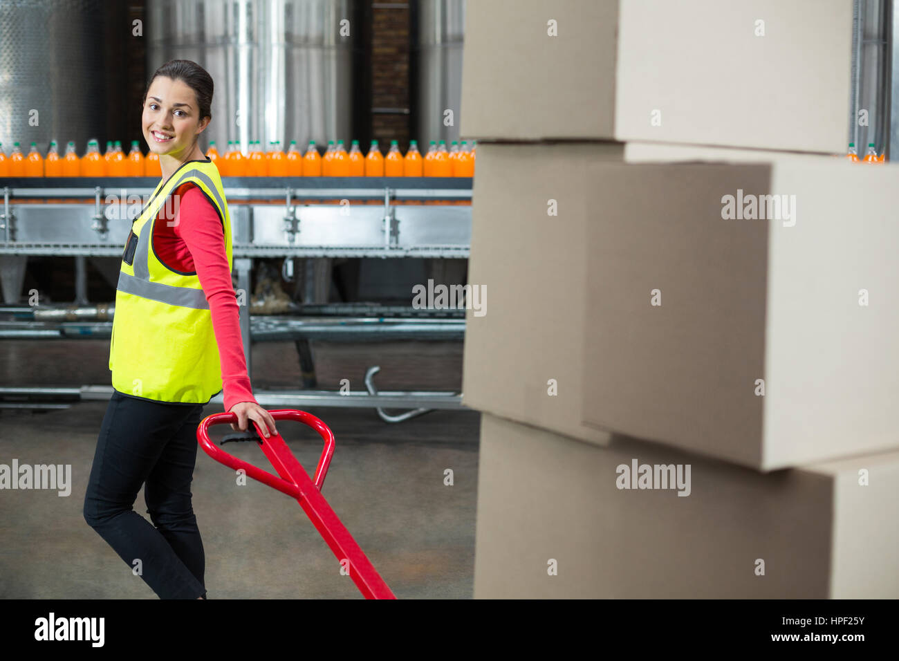Portrait of female factory worker holding trolley of cardboard boxes at ...