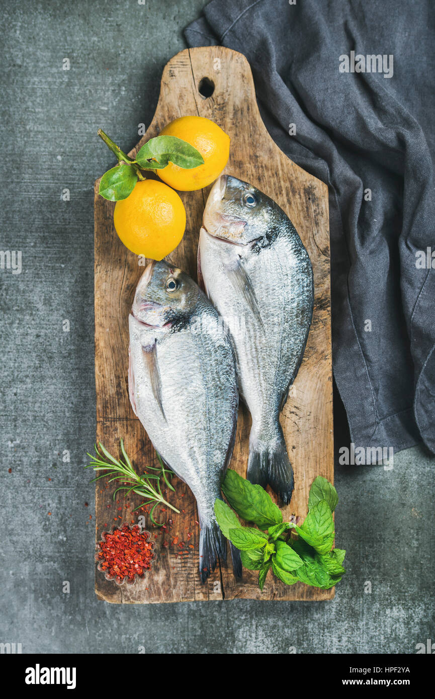 Fresh uncooked sea bream or dorado fish with lemon, herbs and spices on rustic wooden board over grey concrete background, top view. Healthy, dieting, Stock Photo