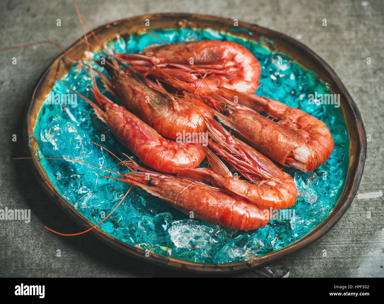 Raw uncooked red shrimps on chipped ice in turquoise blue ceramic tray over grey concrete background, selective focus, horizontal composition. Fresh s Stock Photo